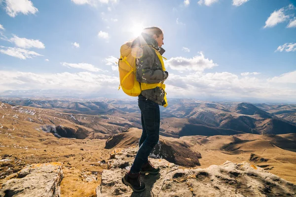 Donna turista con un grande zaino giallo si erge sullo sfondo delle alte montagne in una giornata di sole — Foto Stock