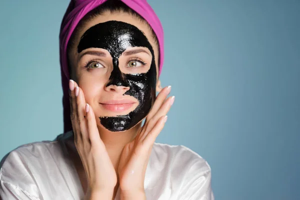 Egy nő, egy törülközőt a fején alkalmazott tisztító maszk arcán fekete — Stock Fotó