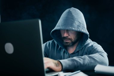 erkek hacker'bir kazak bir kukuleta ile bir dizüstü bilgisayar oturuyor