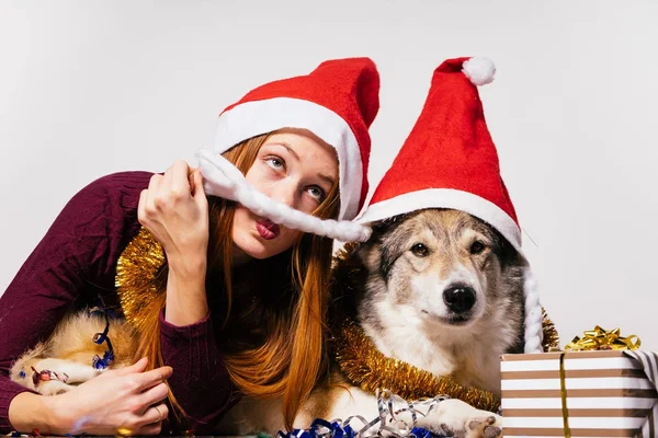 Женщина в новогодней кепке лежит рядом с собакой на фоне подарков — стоковое фото