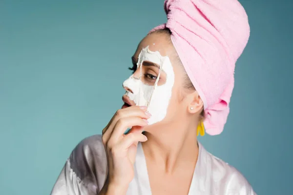 Kobieta z ręcznikiem na głowie kładzie białą maskę na twarzy — Zdjęcie stockowe
