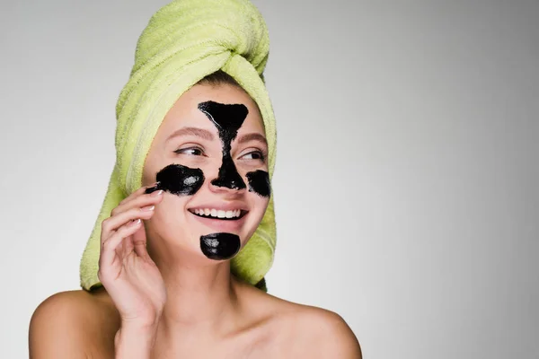 Γυναίκα με μια πετσέτα στο κεφάλι της μια μαύρη μάσκα εφαρμόζεται πάνω στο δέρμα του προσώπου — Φωτογραφία Αρχείου