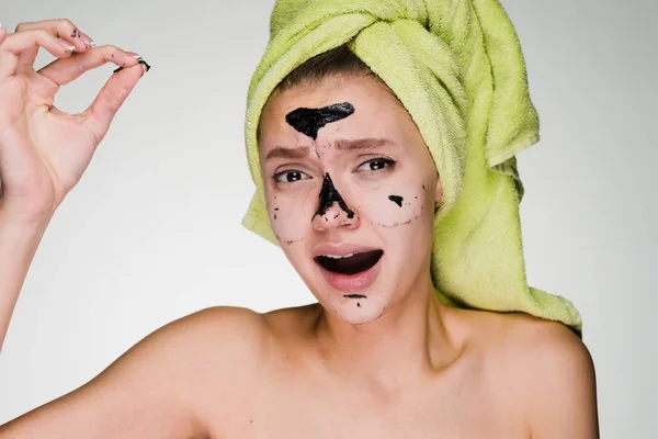 A woman with a towel on her head removes the mask from her face — Stock Photo, Image