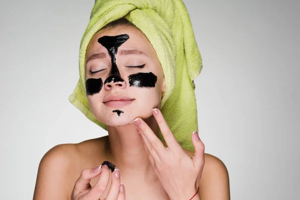 Een vrouw met een handdoek op haar hoofd verwijdert het reinigende masker uit haar gezicht — Stockfoto