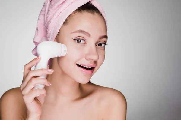 Kvinna med en handduk på huvudet rengör ansiktet med en borste för djuprengöring — Stockfoto