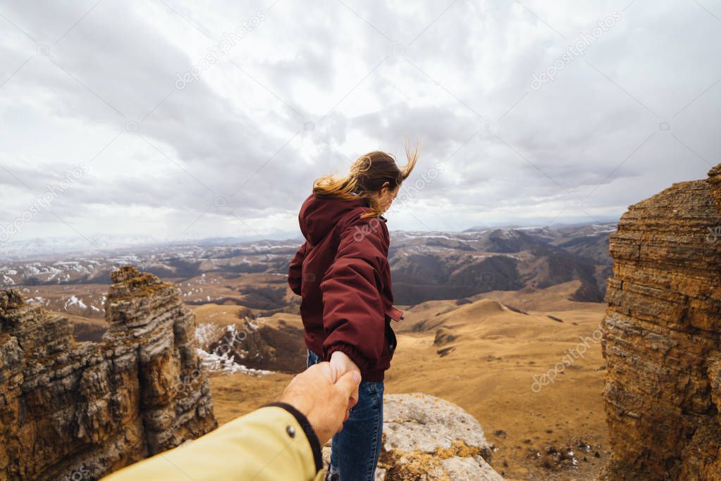 a woman is holding a guy by the hand in the background of the mountains