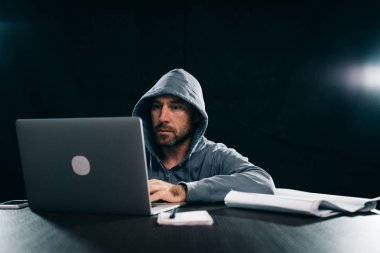 erkek hacker'bir kazak bir kukuleta ile bir dizüstü bilgisayar oturuyor
