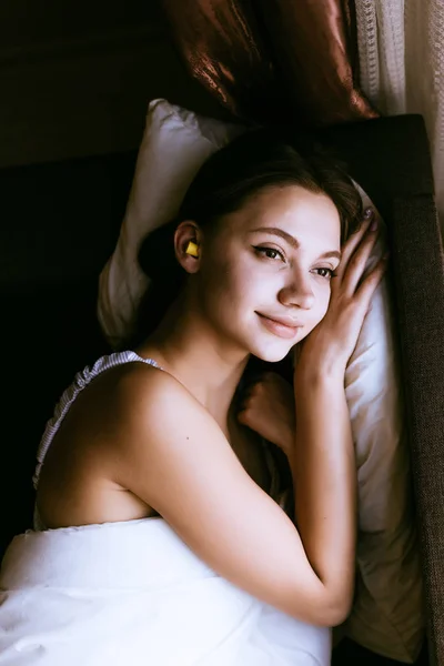 Mulher encontra-se em uma cama com tampões de ouvido — Fotografia de Stock