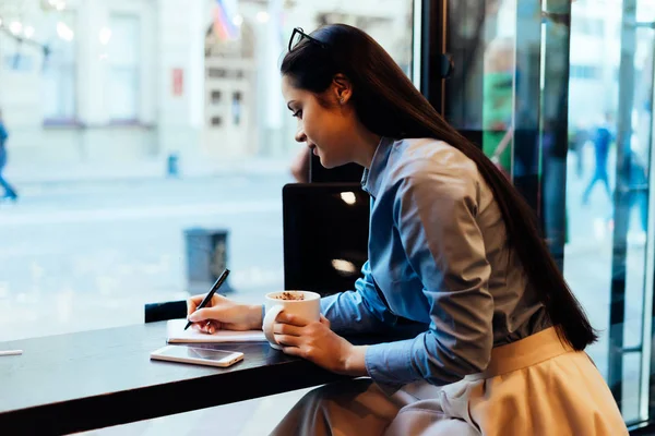 Женщина с длинными волосами сидит за столом и пьет кофе — стоковое фото