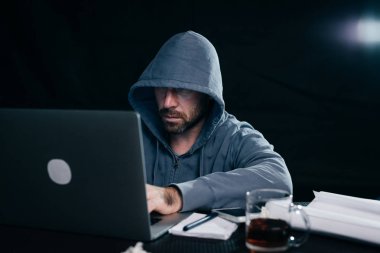 bir adam hacker'bir kazak bir kukuleta ile bir dizüstü bilgisayar oturur ve çay içer