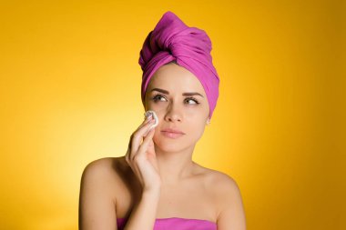 Sarı bir arka plan üzerinde bir pamuk disk ile ona makyaj kapalı başında bir havlu ile bir kadın lazım