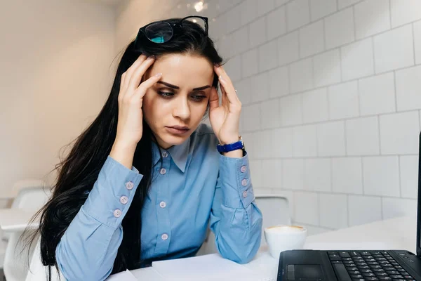 Een gefrustreerde vrouw zit aan een tafel en klampt zich vast aan haar hoofd — Stockfoto