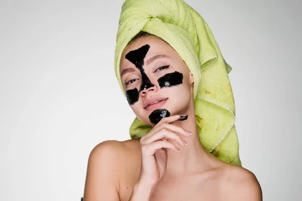 Γυναίκα με μια πετσέτα στο κεφάλι της μια μαύρη μάσκα εφαρμόζεται στις προβληματικές περιοχές του δέρματος του προσώπου — Φωτογραφία Αρχείου