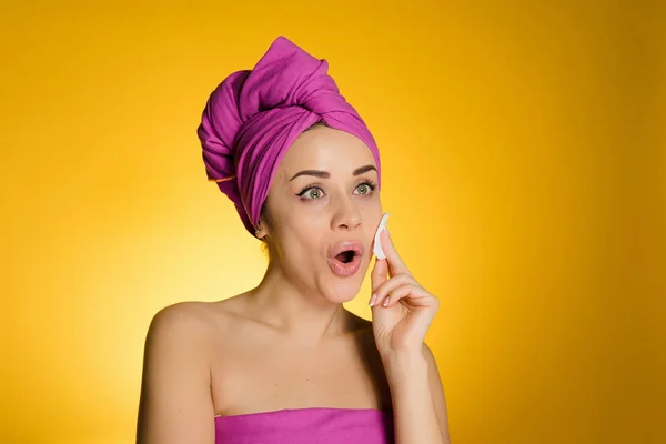 Женщина с полотенцем на голове удаляет макияж с хлопковым диском — стоковое фото