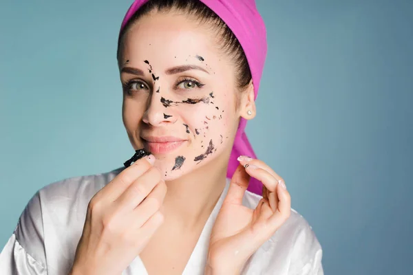 Uma mulher com uma toalha na cabeça remove a máscara de limpeza de seu rosto — Fotografia de Stock