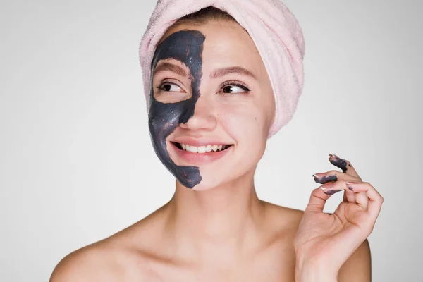 Szczęśliwa kobieta z ręcznikiem na głowie na szarym tle stosować maskę oczyszczający — Zdjęcie stockowe