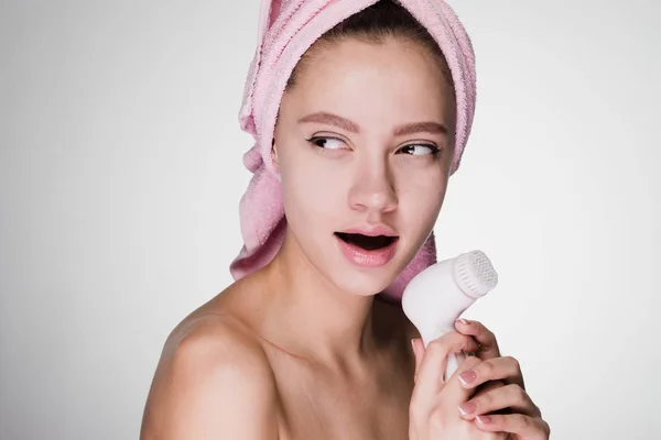 Mulher com uma toalha na cabeça segura uma escova para limpeza profunda da pele — Fotografia de Stock