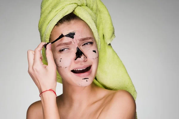 Kvinna med en handduk på huvudet tar bort masken rengör huden i ansiktet — Stockfoto