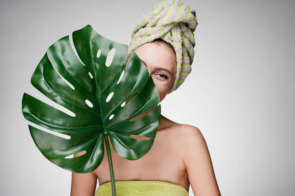 woman with a towel on her head holds in her hand a large leaf