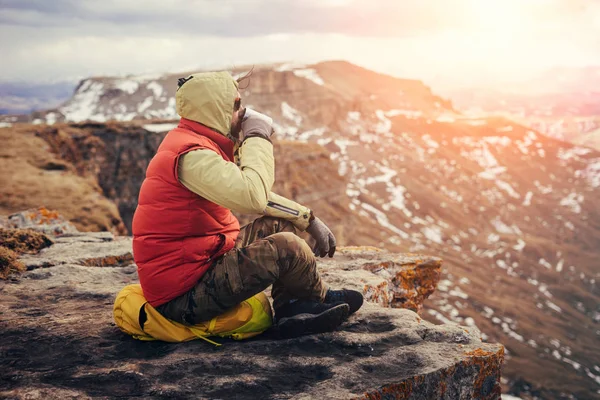 Male tourist sits on the background of mountains and drinks tea — Stock Photo, Image