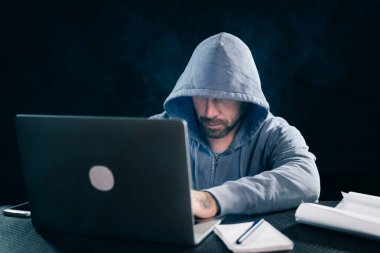 bir kazak bir masada oturan ve laptop arıyorum bir kukuleta ile erkek hacker