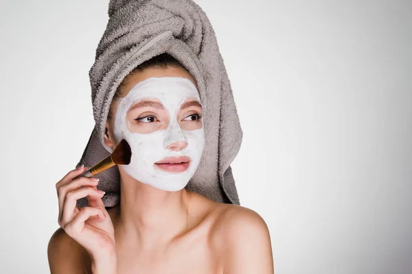 Mujer con una toalla en la cabeza se aplica una máscara blanca de limpieza — Foto de Stock