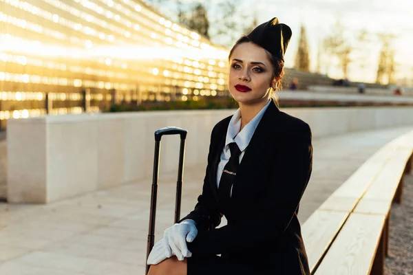 Smutný letuška žena v uniformě sedí vedle kufr — Stock fotografie