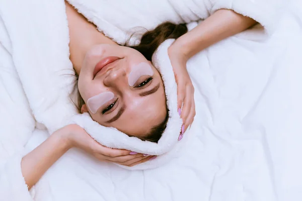 Kobieta leży w szlafrok na łóżko i położyć plastry pod oczy — Zdjęcie stockowe