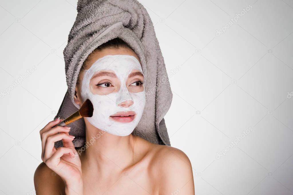 woman with a towel on her head applied a white cleansing mask