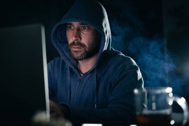 erkek hacker'bir kazak bir kukuleta ile bir dizüstü bilgisayar oturuyor