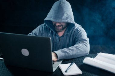 bir adam hacker'bir kazak bir kukuleta ile bir dizüstü bilgisayar ve klavyede yazmaya ne arkasında bir odada oturur