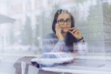 bir kadın gözlük bir masada oturur ve telefonda konuşuyor