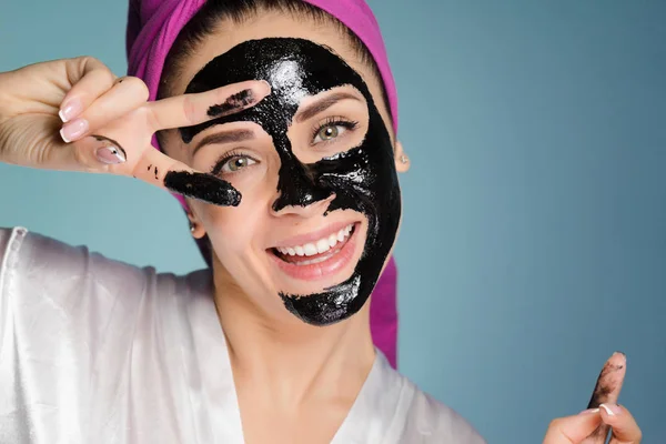 Šťastná žena s ručníkem na hlavě aplikuje masku k čištění pokožky obličeje — Stock fotografie