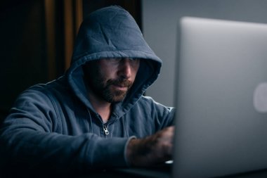 bir adam hacker bir dizüstü bilgisayar arkasında bir odada oturuyor ve bir şey basar