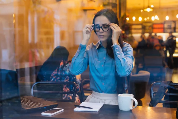 Девушка в очках сидит за столом, пьет кофе — стоковое фото