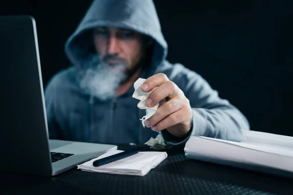 Hacker mâle assis dans une pièce derrière un ordinateur portable y fume — Photo