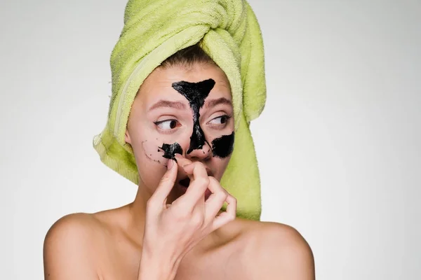 Жінка з рушником на голові знімає маску для обличчя — стокове фото