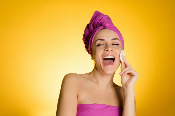 Lycklig kvinna med en handduk på huvudet tar bort makeup med en bomull-skiva — Stockfoto