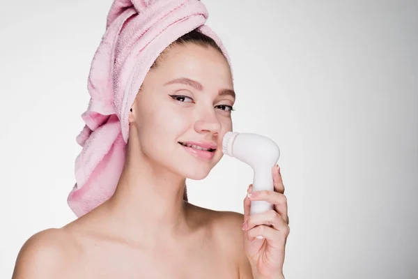 Donna felice con un asciugamano in testa pulisce la pelle del viso con un pennello per una pulizia profonda — Foto Stock