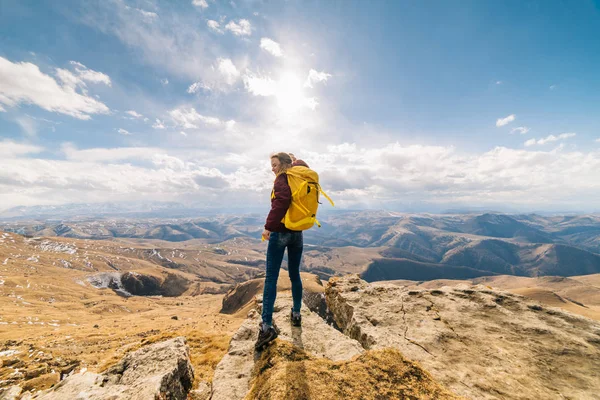 Женщина-туристка с большим рюкзаком стоит посреди высоких гор — стоковое фото