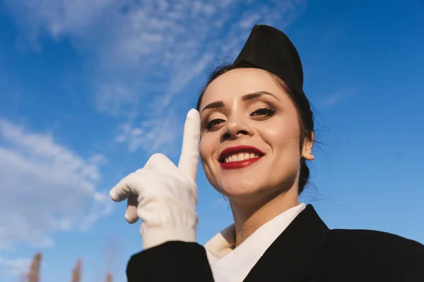 Donna felice hostess in uniforme posa sulla macchina fotografica su sfondo cielo — Foto Stock