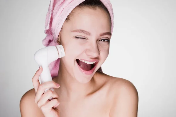 Mulher feliz com uma toalha na cabeça segurando uma escova para limpeza profunda da pele — Fotografia de Stock