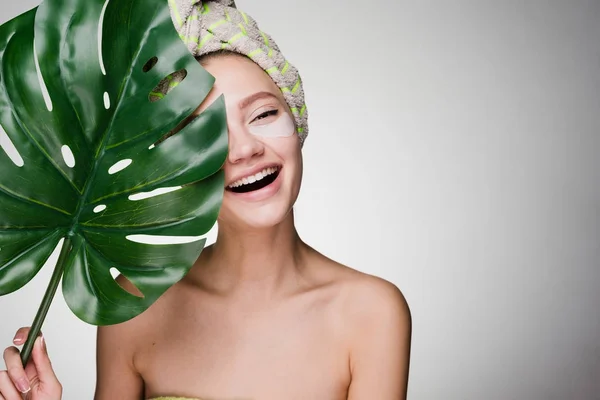 Ευτυχισμένη γυναίκα με μια πετσέτα στο κεφάλι της έχει μπαλώματα και κατέχει ένα μεγάλο φύλλο — Φωτογραφία Αρχείου