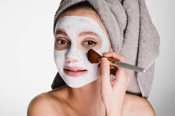 Mulher com uma toalha na cabeça aplica uma máscara facial para limpar o rosto — Fotografia de Stock