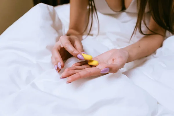 Žena sedí v posteli a držení špunty do uší — Stock fotografie