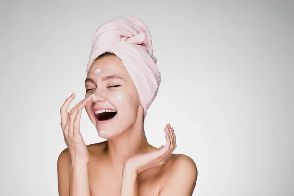 Lycklig kvinna med en handduk på huvudet tillämpa kräm på ansiktet huden — Stockfoto