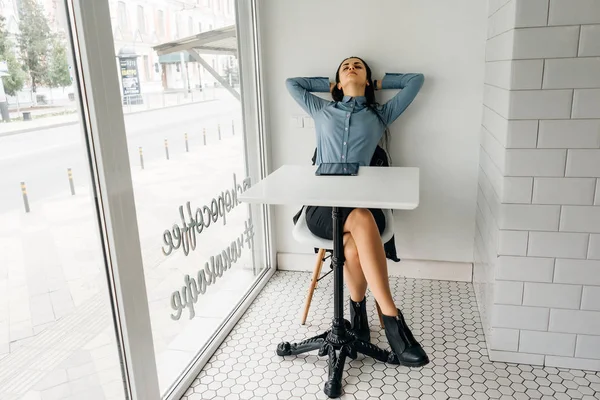 Mujer cansada sentada en una mesa frente a una gran ventana — Foto de Stock