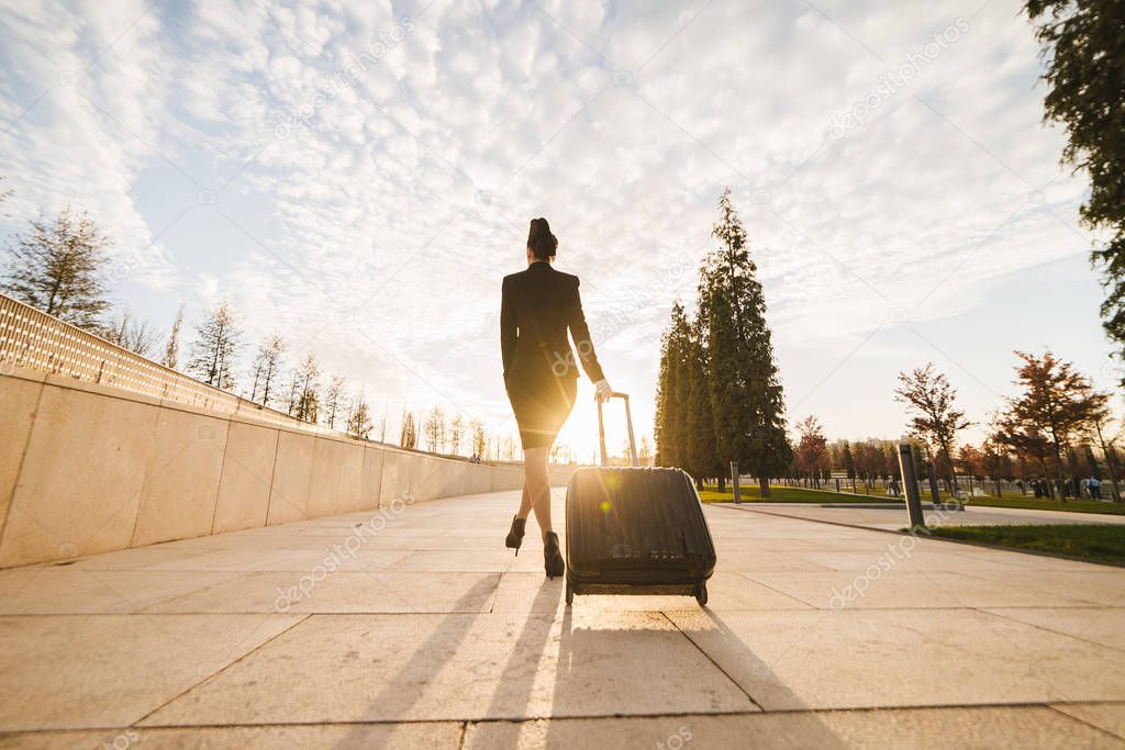 A female flight attendant in uniform carries a large black suitcase