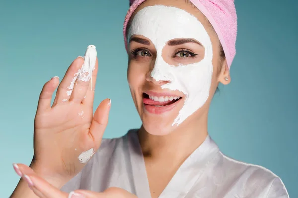 Ευτυχισμένη γυναίκα με μια πετσέτα στο κεφάλι εφαρμόστε μια μάσκα καθαρισμού στο δέρμα του προσώπου — Φωτογραφία Αρχείου