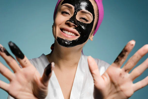 Donna felice con un asciugamano sulla testa applicato una maschera alla pelle del suo viso — Foto Stock